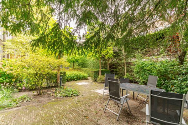Groene, beschutte stadstuin aan het Lange Voorhout met een terras en tuintafel met stoelen.